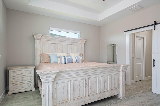 bedroom with a barn door, a tray ceiling, and baseboards