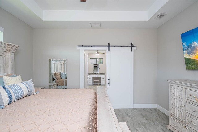 bedroom with a barn door, a raised ceiling, and baseboards