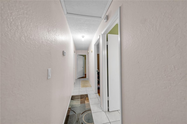 hall featuring a textured wall, light tile patterned floors, and a textured ceiling