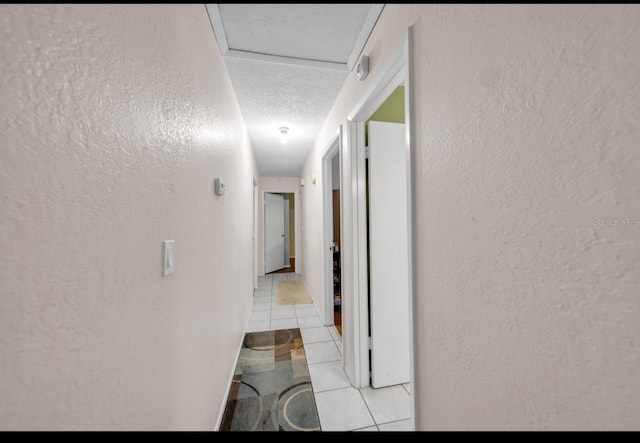 hallway with a textured wall, light tile patterned floors, and a textured ceiling