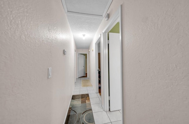 corridor with a textured wall, light tile patterned flooring, and a textured ceiling
