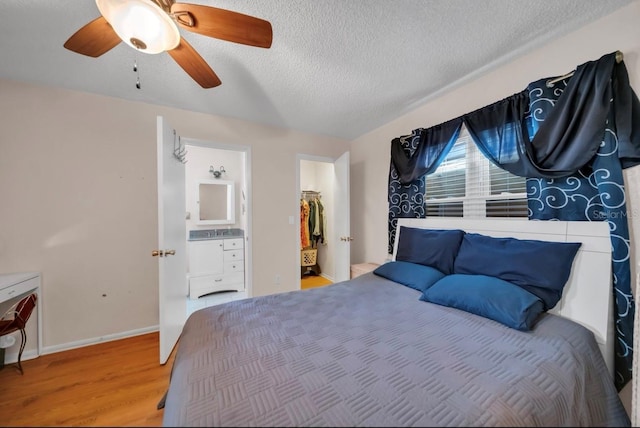 bedroom featuring wood finished floors, a walk in closet, a textured ceiling, a ceiling fan, and a closet