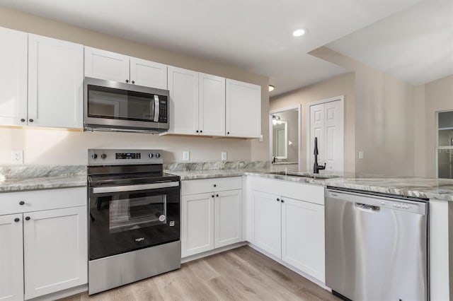 2381 Sheila Ln, North Port, FL 34286 - kitchen with stainless steel appliances, a sink, a peninsula, white cabinetry, and light wood-type flooring