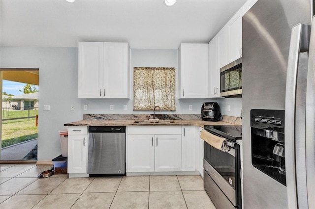 kitchen featuring appliances with stainless steel finishes, a sink, light tile patterned flooring, and white cabinets
