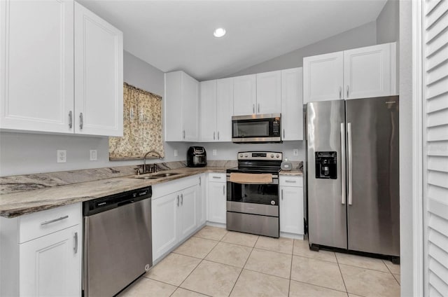 kitchen featuring stainless steel appliances, a sink, lofted ceiling, white cabinets, and light stone counters