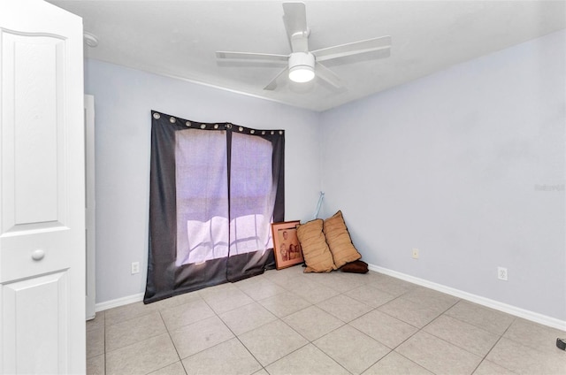 tiled empty room with ceiling fan and baseboards