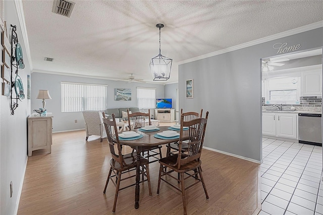 dining area featuring ceiling fan, light wood-style flooring, crown molding, a textured ceiling, and baseboards