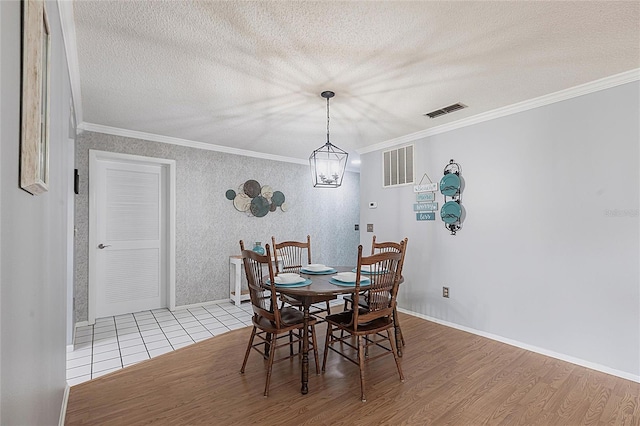 dining area featuring wood finished floors, ornamental molding, a textured ceiling, baseboards, and wallpapered walls