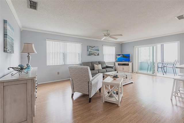 living room with a textured ceiling, ornamental molding, light wood-style flooring, ceiling fan, and baseboards