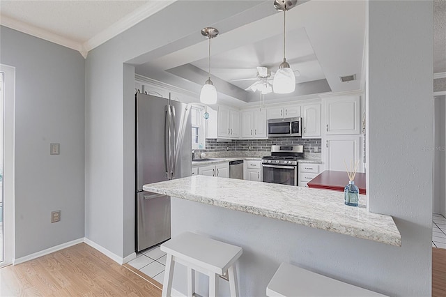 kitchen featuring appliances with stainless steel finishes, a peninsula, light wood-style flooring, white cabinetry, and ornamental molding