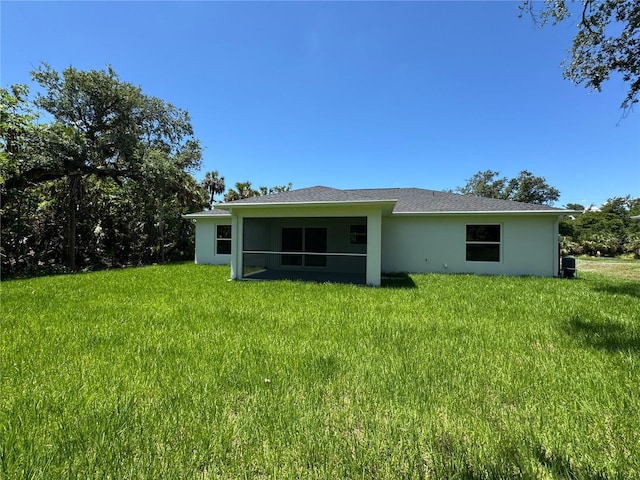 rear view of house featuring a lawn, stucco siding, and a sunroom