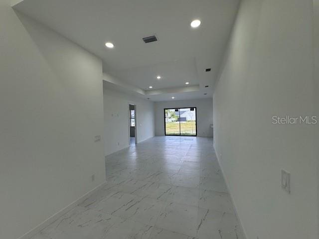 hall with recessed lighting, baseboards, light marble finish floors, and a raised ceiling