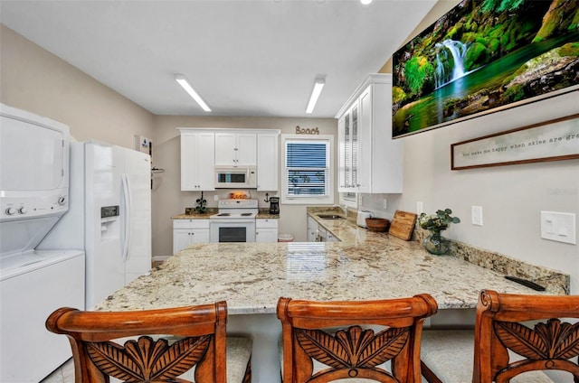 4231 Hollis Ave, Port Charlotte, FL 33953 - kitchen with white appliances, stacked washer / drying machine, a peninsula, white cabinetry, and light stone countertops