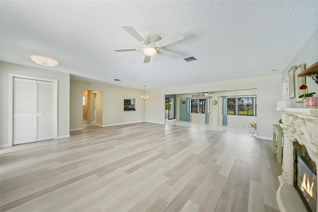 16615 Acapulco Rd, Punta Gorda, FL 33955 - unfurnished living room featuring a glass covered fireplace, a textured ceiling, a chandelier, ceiling fan, and light wood-type flooring