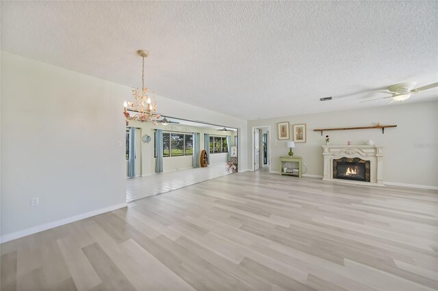 16615 Acapulco Rd, Punta Gorda, FL 33955 - unfurnished living room with a textured ceiling, a chandelier, light wood-type flooring, a lit fireplace, and ceiling fan