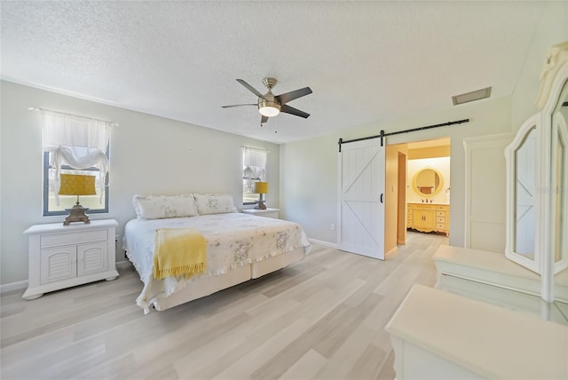 16615 Acapulco Rd, Punta Gorda, FL 33955 - bedroom with a barn door, light wood-style floors, a textured ceiling, baseboards, and ceiling fan
