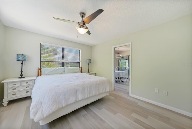 16615 Acapulco Rd, Punta Gorda, FL 33955 - bedroom with a chandelier, light wood-style floors, a ceiling fan, baseboards, and a textured ceiling
