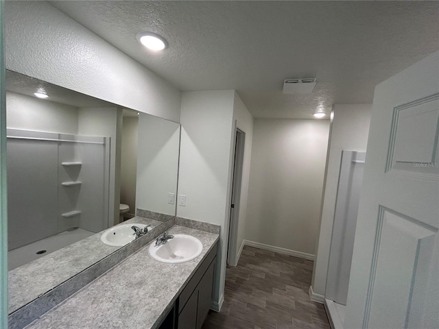 bathroom with a textured ceiling, a shower, toilet, vanity, and baseboards