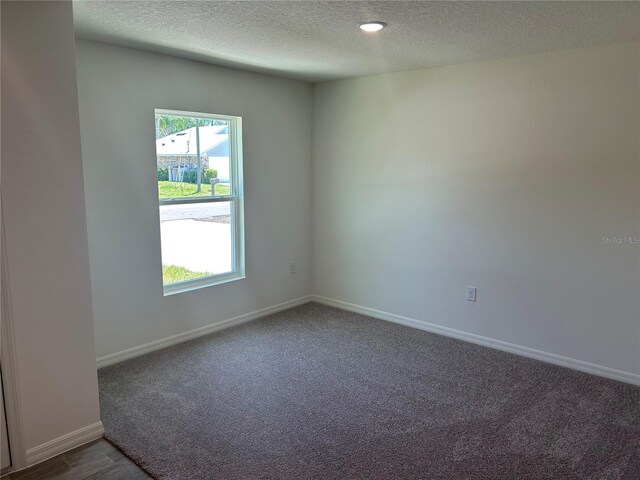 empty room featuring a textured ceiling, plenty of natural light, baseboards, and dark carpet