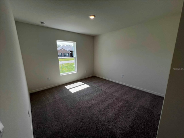 unfurnished room with dark colored carpet and baseboards