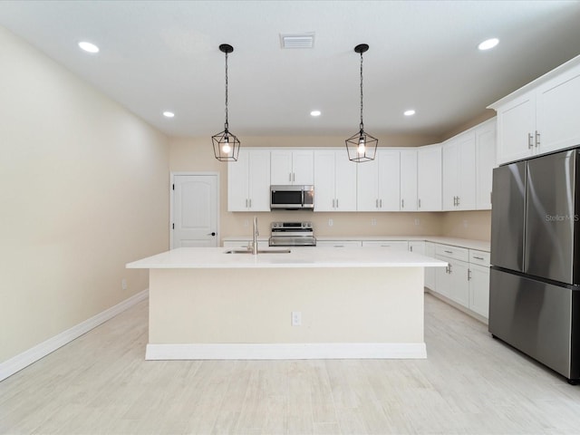 kitchen with stainless steel appliances, a sink, baseboards, a kitchen island with sink, and light countertops