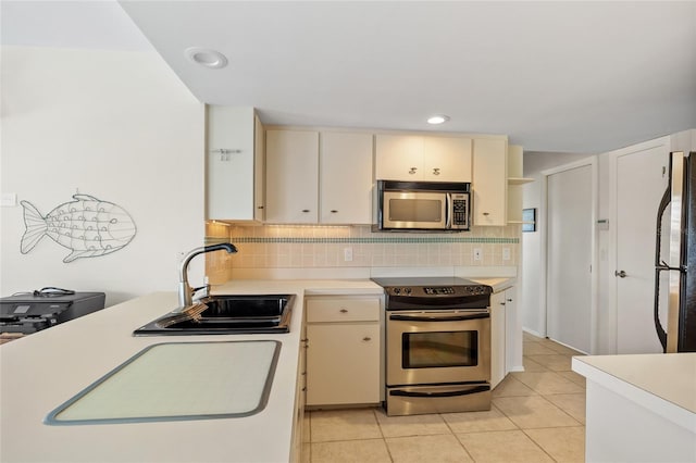 kitchen featuring appliances with stainless steel finishes, a sink, cream cabinetry, light countertops, and backsplash