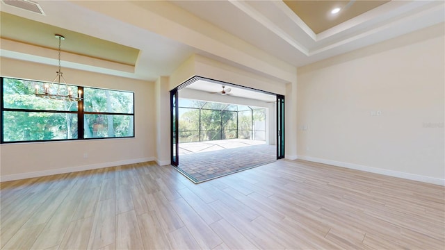 empty room with a raised ceiling, light wood-style floors, baseboards, and a chandelier