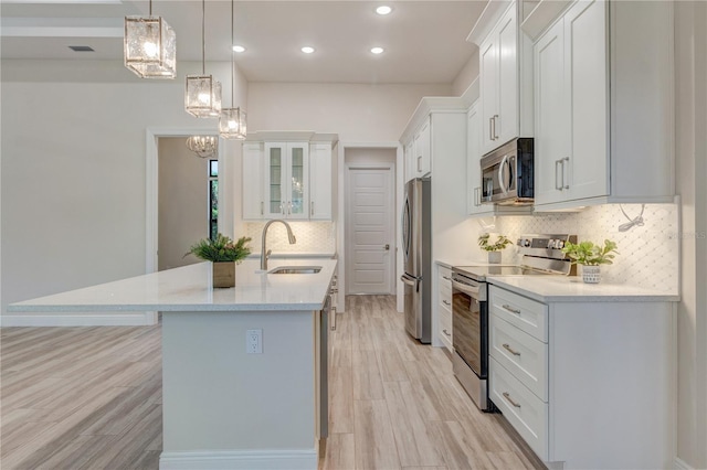 kitchen with appliances with stainless steel finishes, a sink, decorative backsplash, a kitchen island with sink, and white cabinetry