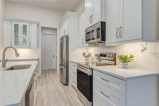 kitchen with appliances with stainless steel finishes, a sink, decorative backsplash, and white cabinetry