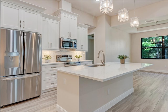 kitchen with stainless steel appliances, a chandelier, a sink, an island with sink, and backsplash