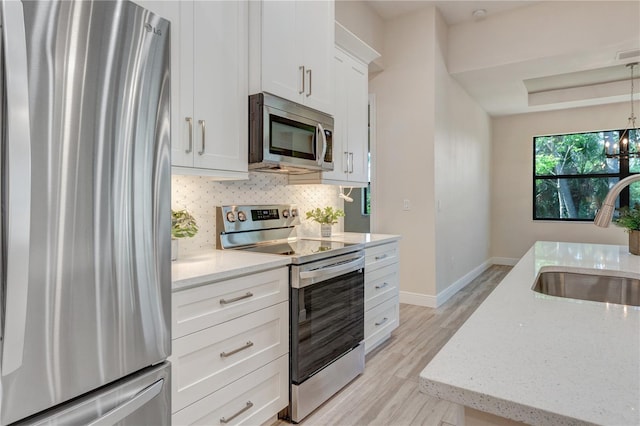 kitchen featuring appliances with stainless steel finishes, a sink, light wood-style floors, white cabinetry, and light stone counters
