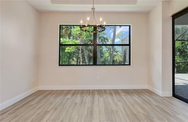 empty room featuring a chandelier, light wood finished floors, a raised ceiling, and baseboards