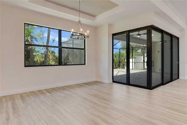 unfurnished room with a tray ceiling, a chandelier, baseboards, and wood finished floors