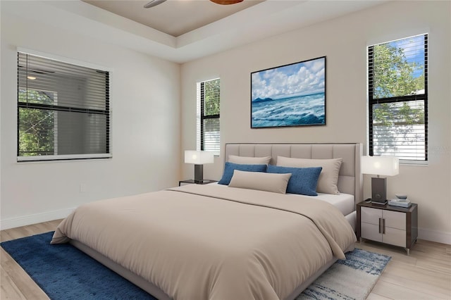 bedroom with baseboards, light wood-style floors, and a tray ceiling