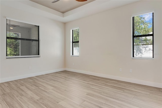 unfurnished room featuring light wood-style floors, ceiling fan, baseboards, and a raised ceiling