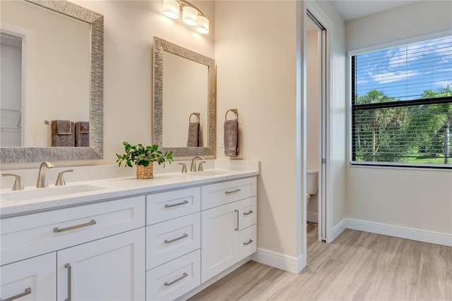 full bathroom with double vanity, wood finished floors, toilet, and baseboards