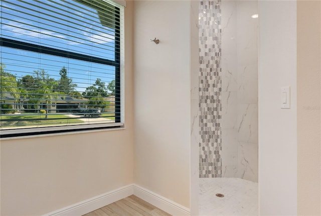 full bathroom with a marble finish shower, baseboards, and wood finished floors