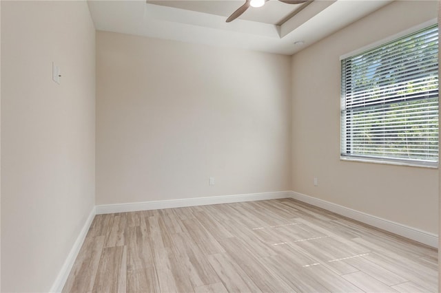 unfurnished room featuring a tray ceiling, light wood-type flooring, a ceiling fan, and baseboards