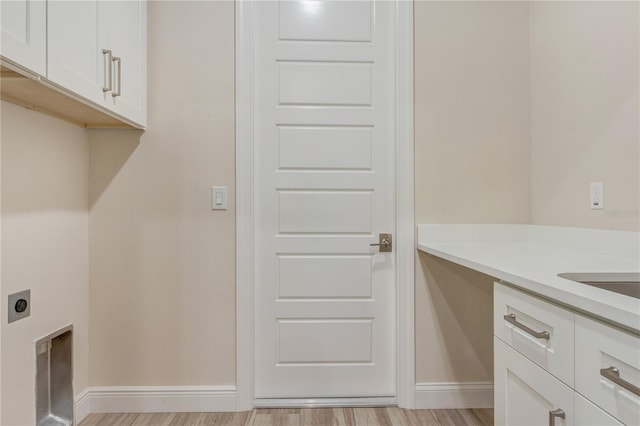 clothes washing area with hookup for an electric dryer, cabinet space, light wood-type flooring, and baseboards