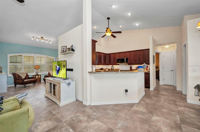 kitchen with stainless steel microwave, a ceiling fan, light stone counters, a peninsula, and open floor plan
