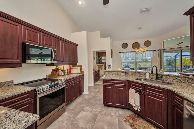 kitchen with stainless steel appliances, a sink, reddish brown cabinets, a chandelier, and vaulted ceiling
