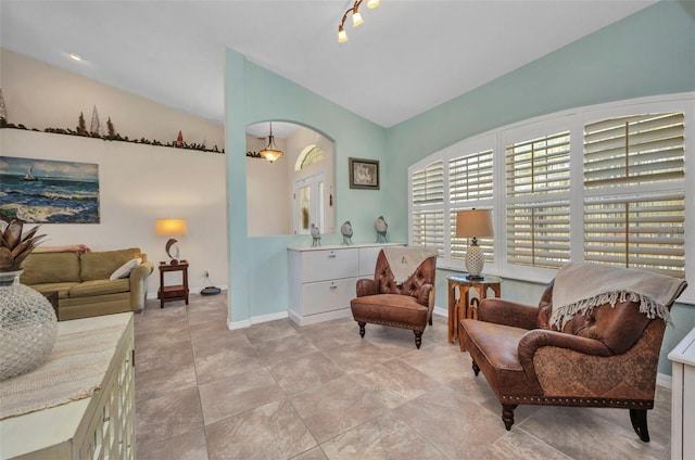 sitting room featuring lofted ceiling, arched walkways, and baseboards