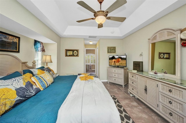 bedroom featuring a tray ceiling, dark tile patterned floors, and a ceiling fan
