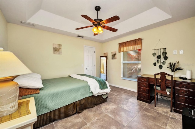 bedroom featuring a raised ceiling, baseboards, a ceiling fan, and a desk