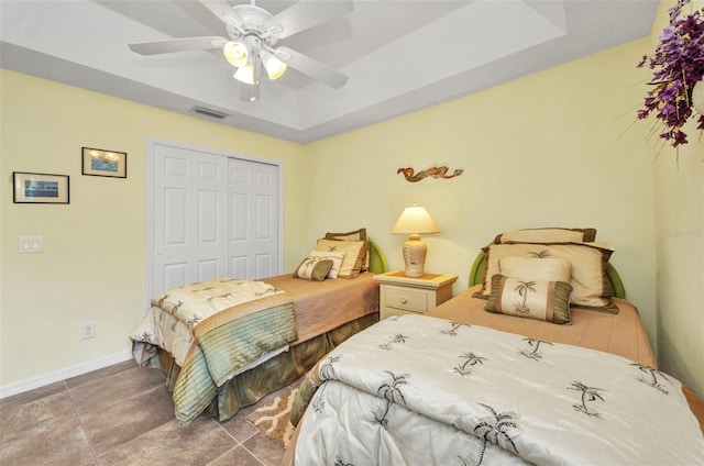 tiled bedroom with a closet, baseboards, ceiling fan, and a tray ceiling