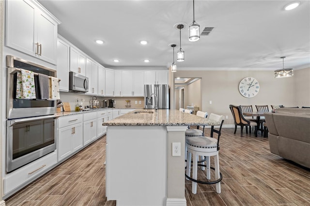25308 Rupert Rd, Punta Gorda, FL 33983 - kitchen featuring stainless steel appliances, a kitchen breakfast bar, wood finish floors, white cabinetry, and ornamental molding