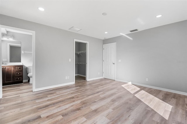 unfurnished bedroom with a walk in closet, light wood-style flooring, baseboards, a closet, and recessed lighting