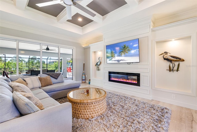 living area featuring a ceiling fan, coffered ceiling, crown molding, beam ceiling, and a glass covered fireplace