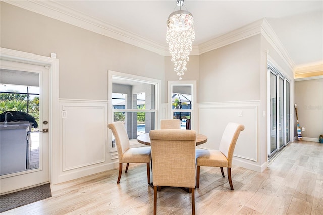 dining area with light wood-style flooring, a chandelier, crown molding, a wainscoted wall, and a decorative wall