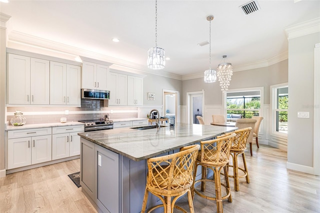 kitchen with a sink, appliances with stainless steel finishes, a chandelier, an island with sink, and a kitchen breakfast bar